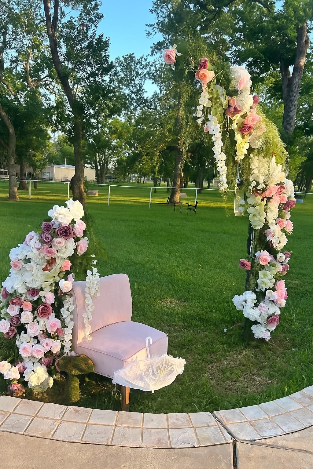 Outdoor floral arch framing a blush chair on a lawn at golden hour